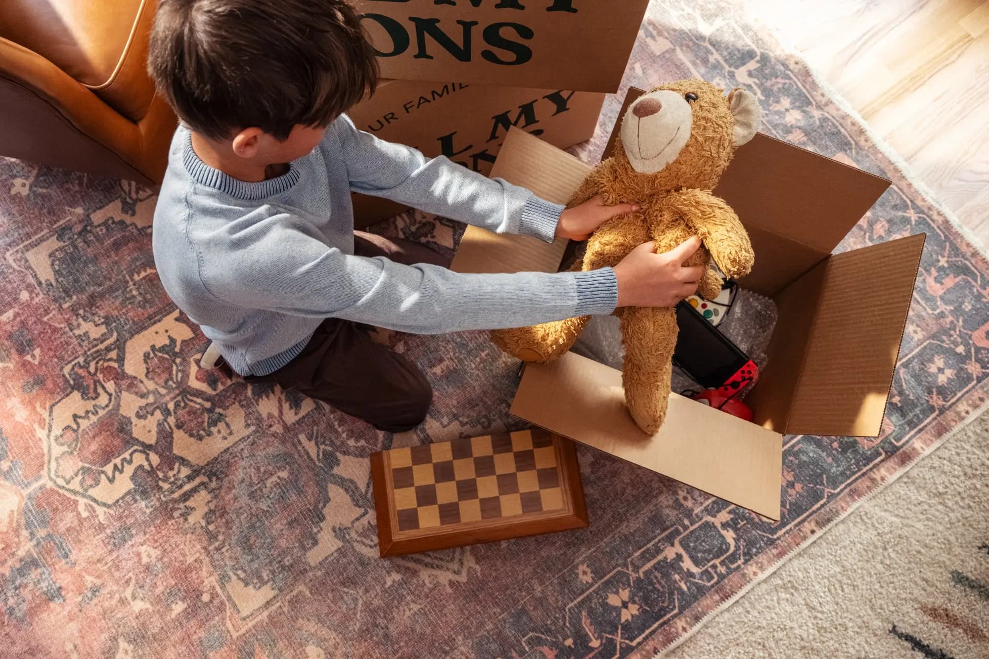 A young boy packs a teddy bear into an All My Sons Moving and Storage box.